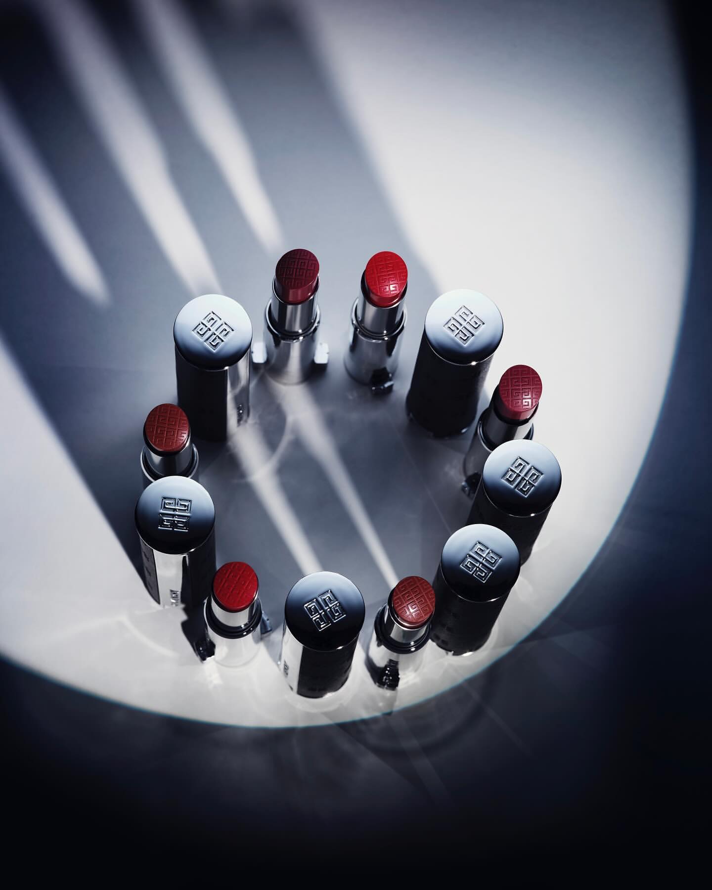 Elevated shot of Givenchy lipsticks arranged in a circle, featuring metallic cases and red lipstick tips, against a softly lit background.