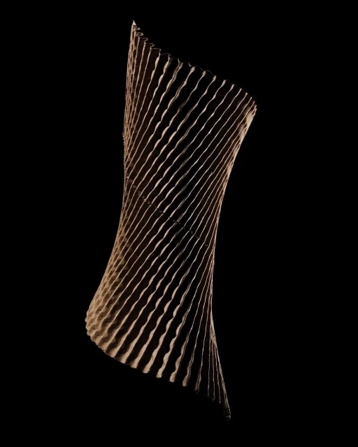 Twisted, vertically-oriented geometric sculpture on black. The sculpture is made of grooved tan material and has a helical shape.