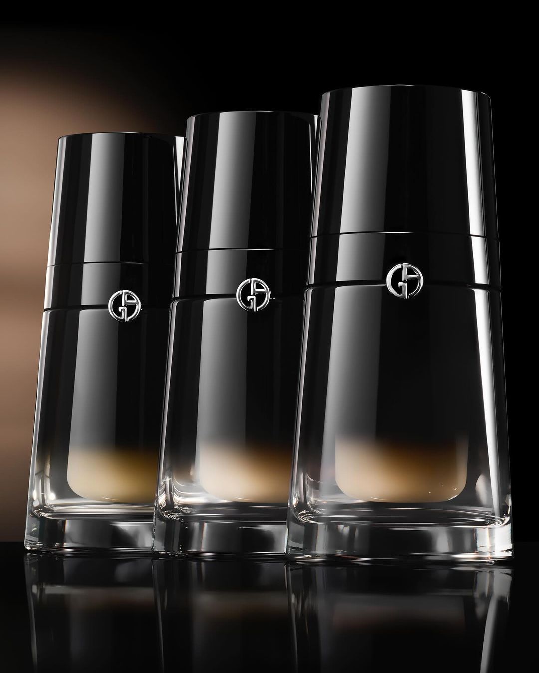 Three Giorgio Armani black-capped glass bottles are aligned on a dark surface, showcasing beauty product packaging with sleek design.