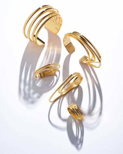 Close-up studio shot of five gold metal cuff bracelets and rings with shadows on a white background. Fashion jewelry product shot.