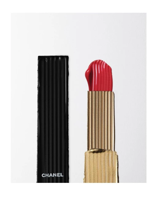Studio shot of open Chanel lipstick with the lid to the side, bright red lipstick and golden container, isolated on white.