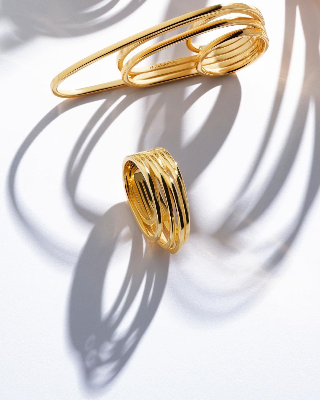 Elevated view of two gold, multi-band rings on a white surface, casting curved shadows, perfect for jewelry and luxury branding.