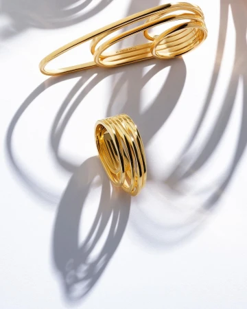 Elevated view of two gold, multi-band rings on a white surface, casting curved shadows, perfect for jewelry and luxury branding.