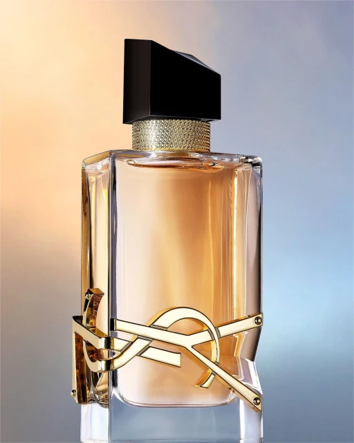 Close-up studio shot of a luxurious perfume bottle with a black cap and gold accents against a gradient orange and blue background.