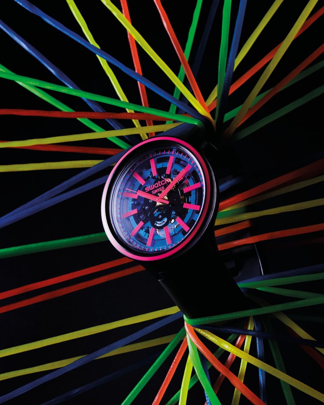 Swatch watch on black background with multiple colored elastic bands wrapped around the watch. Close up studio shot.
