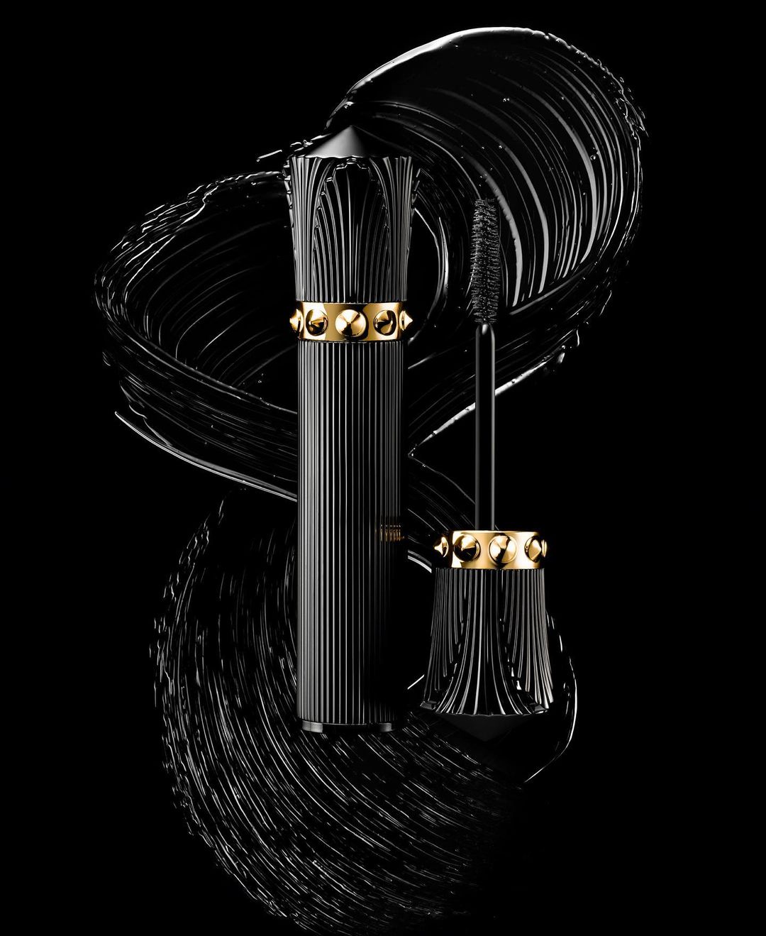 Studio shot of mascara tube with cap off and wand out, surrounded by smear of product, black and gold colors, beauty product shot.