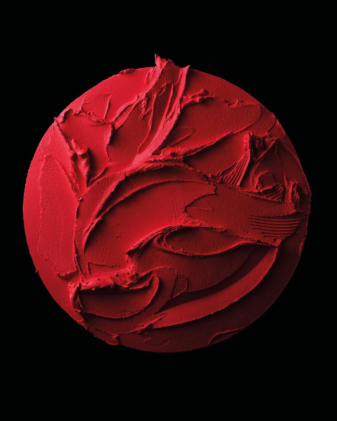 Close-up of vibrant red cosmetic product with textured, smeared surface on a solid black background, accentuating texture and color.