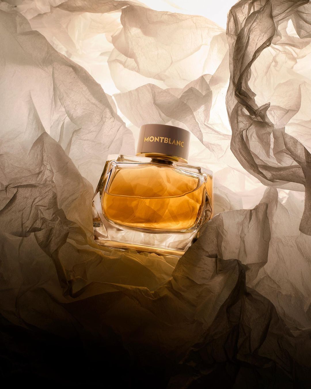 Montblanc perfume bottle on a crumpled tissue paper background, showcasing its amber liquid and elegant design in a studio setting.