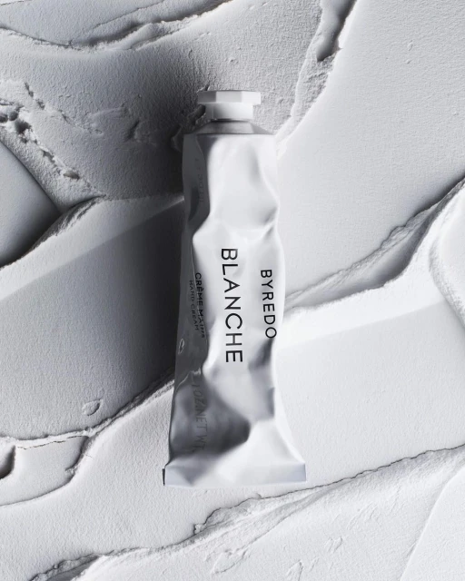 Close-up of Byredo Blanche hand cream tube on textured white background, promoting beauty and personal care products.