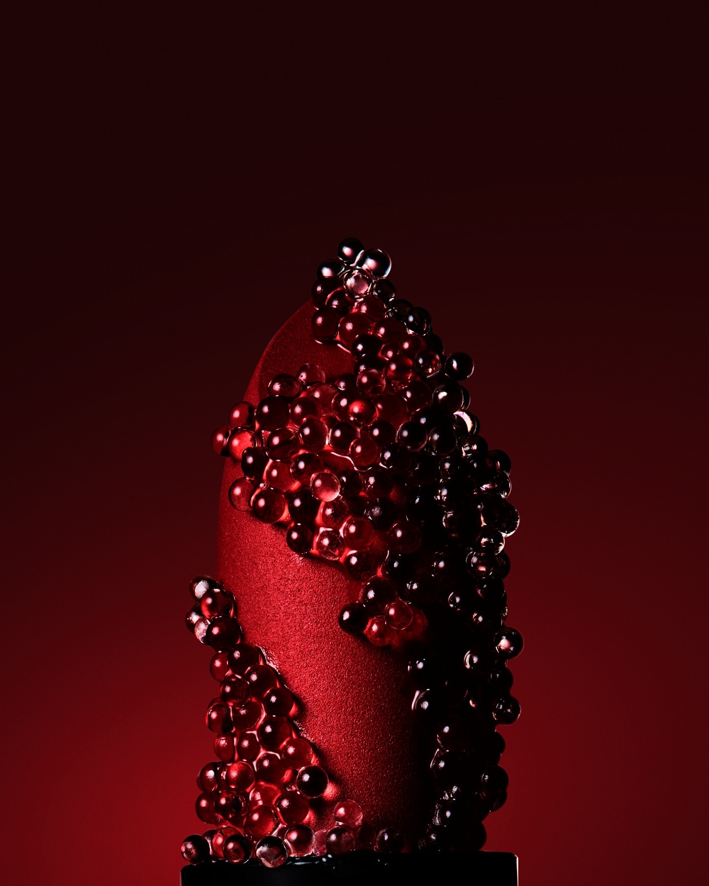 Striking close-up of an abstract red dessert covered in translucent red spheres against a graduated red background.