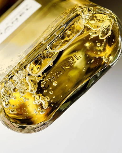 Close-up of a Chanel perfume bottle, revealing the brand name embossed in the glass with golden liquid and bubbles inside the container.