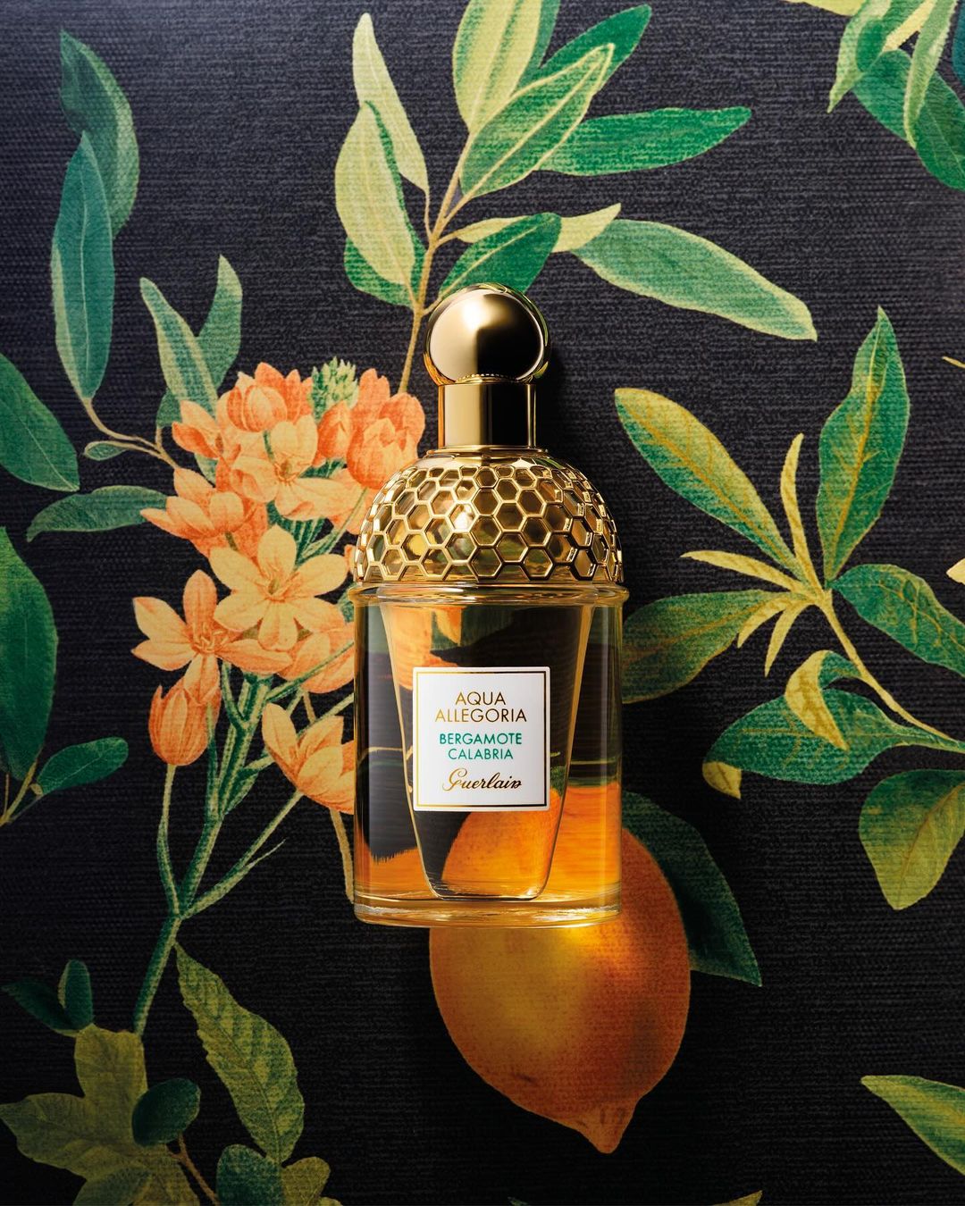 Guerlain Aqua Allegoria Bergamote Calabria fragrance bottle sits atop a lemon with a floral leaf-patterned background in a beauty shot.