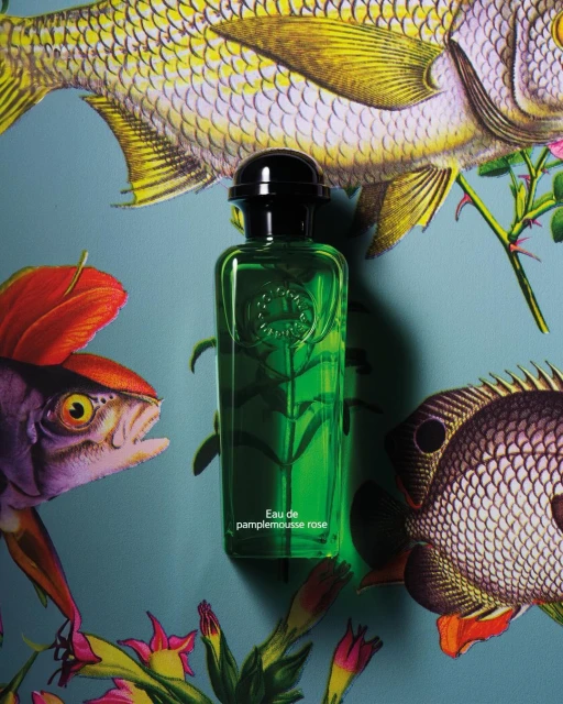 Eau de pamplemousse rose perfume bottle on a light-blue backdrop with colorful fish and floral illustrations for a product shot.