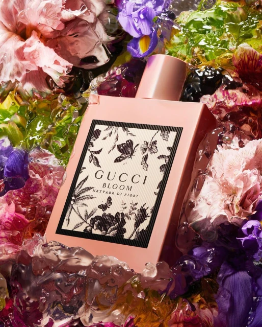 Gucci Bloom Nettare di Fiori perfume bottle surrounded by colorful flowers and ice. Beauty shot for product advertising.