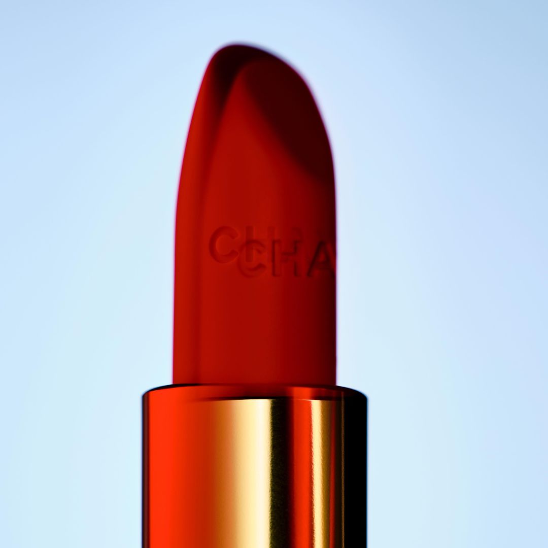 Close-up of a vibrant red lipstick with a gold base against a soft gradient background. Beauty shot for cosmetic promotion.