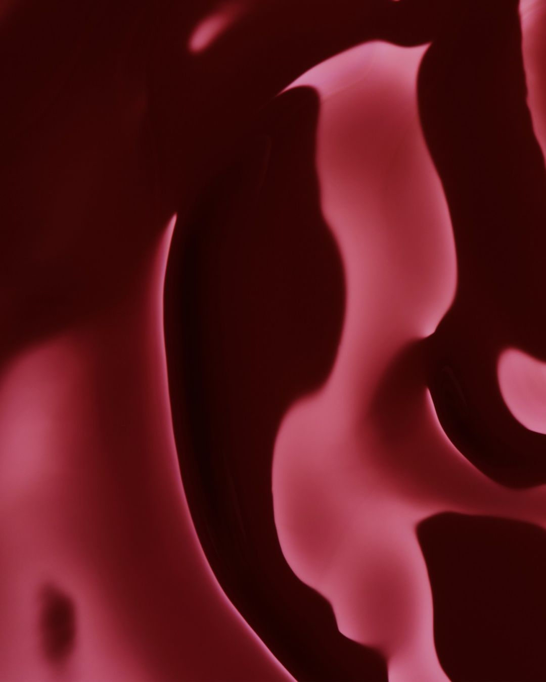 Abstract maroon colored background with wavy shapes and subtle light variations, creating a soft, textured visual effect.