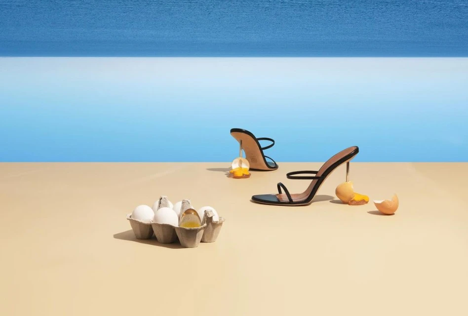 High heels and egg yolks create a surreal fashion still life on a seamless tan surface with ocean backdrop for beauty or advertising.