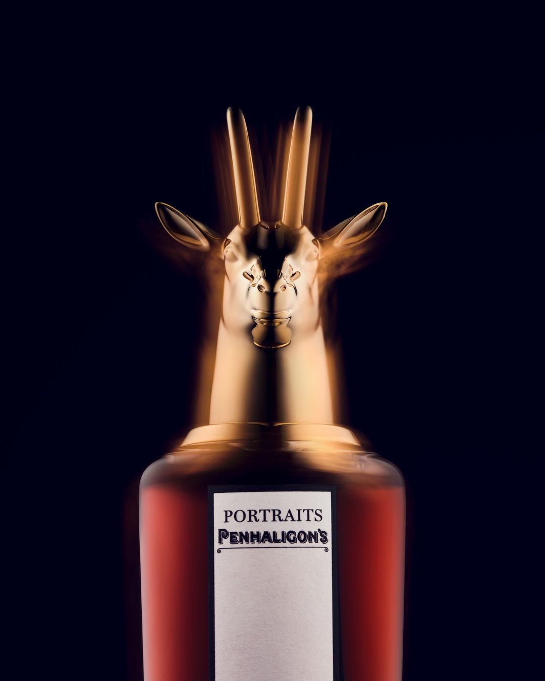 A bottle of Penhaligon's Portraits perfume with a gold antelope head stopper against a dark background, beauty and luxury concept.