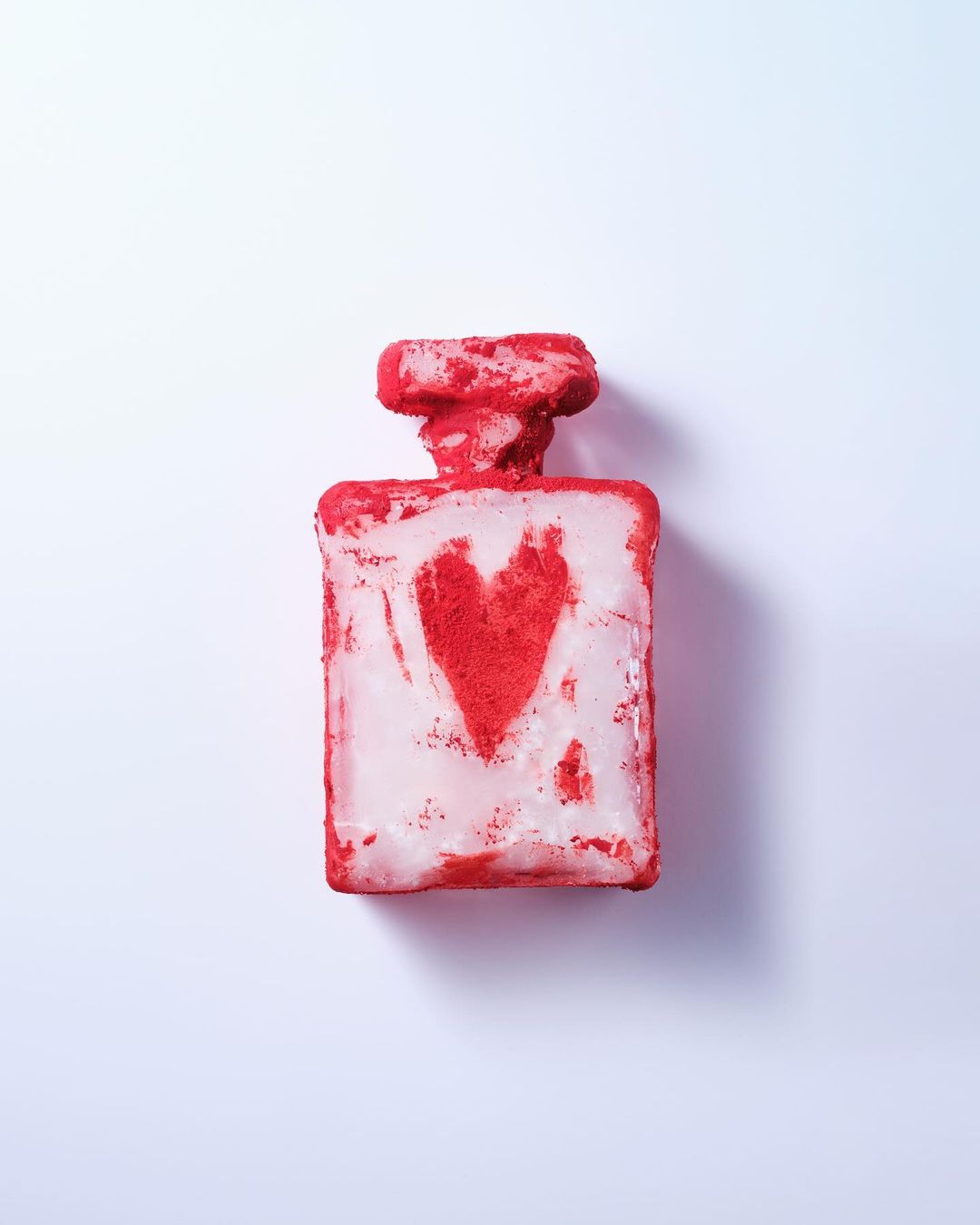 Perfume bottle with red heart design, photographed on a white background, showcasing a textured surface and distinctive packaging.