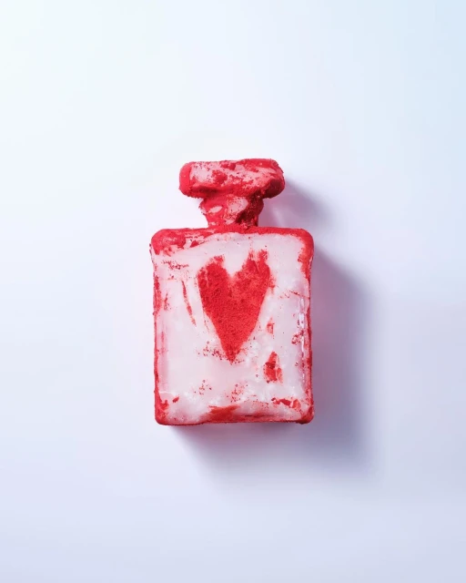 Perfume bottle with red heart design, photographed on a white background, showcasing a textured surface and distinctive packaging.