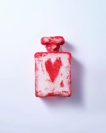 Perfume bottle with red heart design, photographed on a white background, showcasing a textured surface and distinctive packaging.