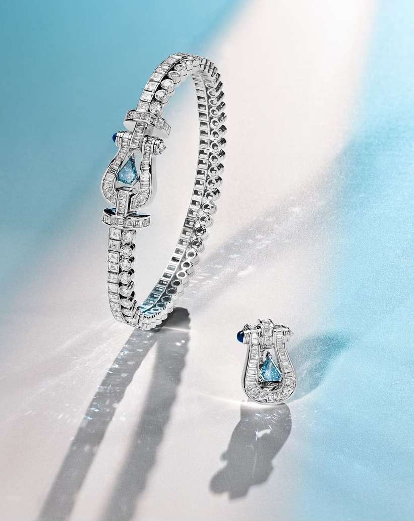 Close-up of a silver bracelet and earring set with light blue gemstones on a light blue and white gradient background with dramatic lighting.