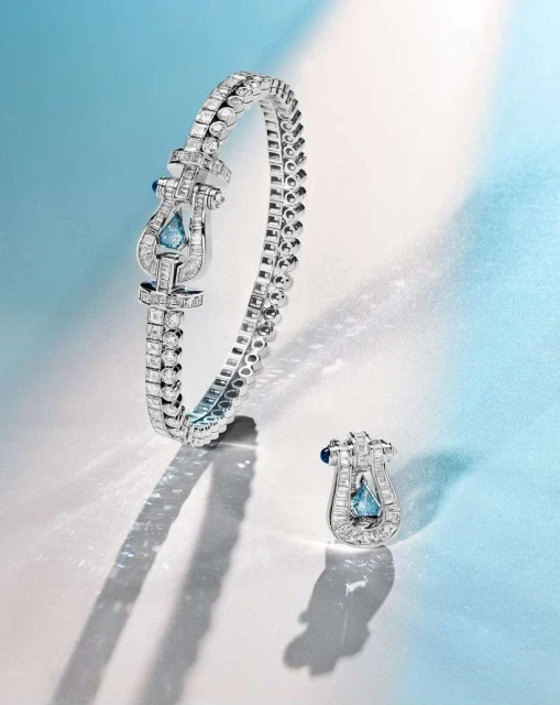 Close-up of a silver bracelet and earring set with light blue gemstones on a light blue and white gradient background with dramatic lighting.