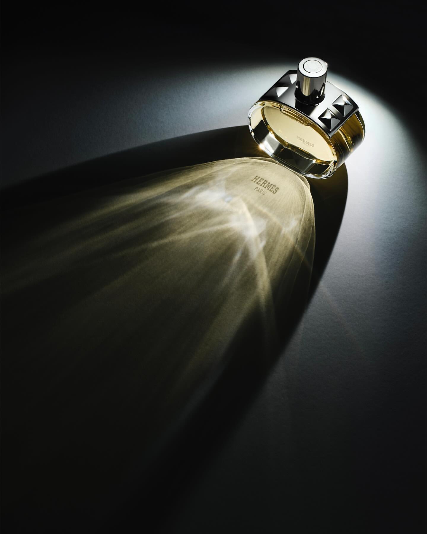 Elegant studio shot of a Hermès Paris fragrance bottle with silver and gold accents, illuminated by a focused light source.