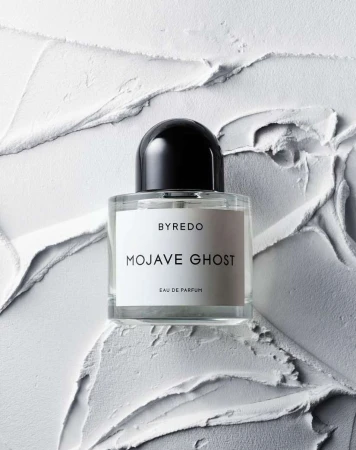 Close-up of a Byredo Mojave Ghost perfume bottle with a black cap against a white textured background. Beauty, fragrance, product shot.