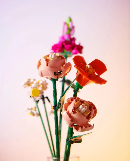 Close-up still life of a colorful bouquet of artificial LEGO flowers in full bloom with orange, pink, and white petals.