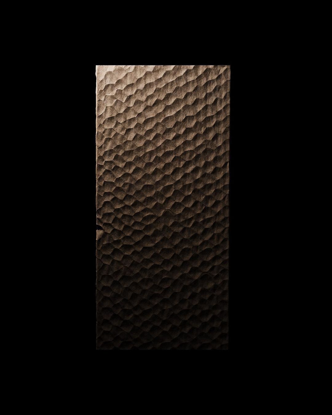 Close-up of a textured, brown wooden surface with an irregular, bumpy pattern, illuminated on the left against a black background.