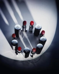A circle of lipstick tubes arranged on a white surface under dramatic spotlight illumination by photographer Lucie Conrad