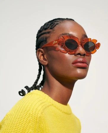 Portrait of a black woman wearing orange sunglasses and a yellow sweater against a white background