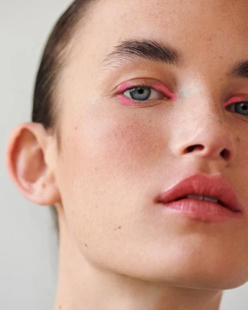 Close-up of a woman's face with light skin and pink eyeliner, focusing on the eyes, nose, and mouth in a beauty or fashion context.
