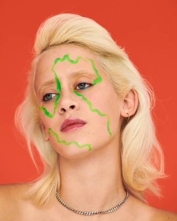 Portrait of a blonde woman with green paint graphic lines on her face against a solid red background