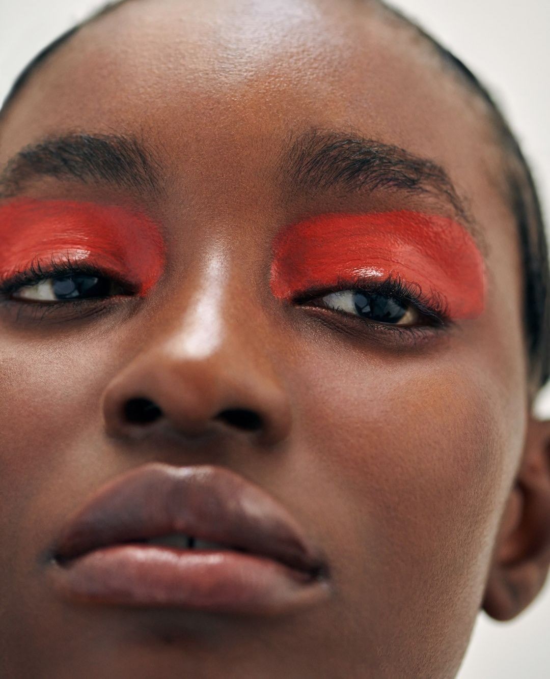 Extreme close-up portrait of a Black woman featuring bold red eyeshadow paint across her eyelids by photographer Lucie Hugary.