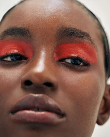 Extreme close-up portrait of a Black woman featuring bold red eyeshadow paint across her eyelids by photographer Lucie Hugary.