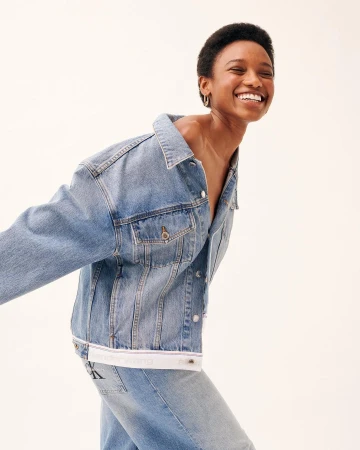 Smiling Black woman wearing a blue denim jacket against a bright seamless white background