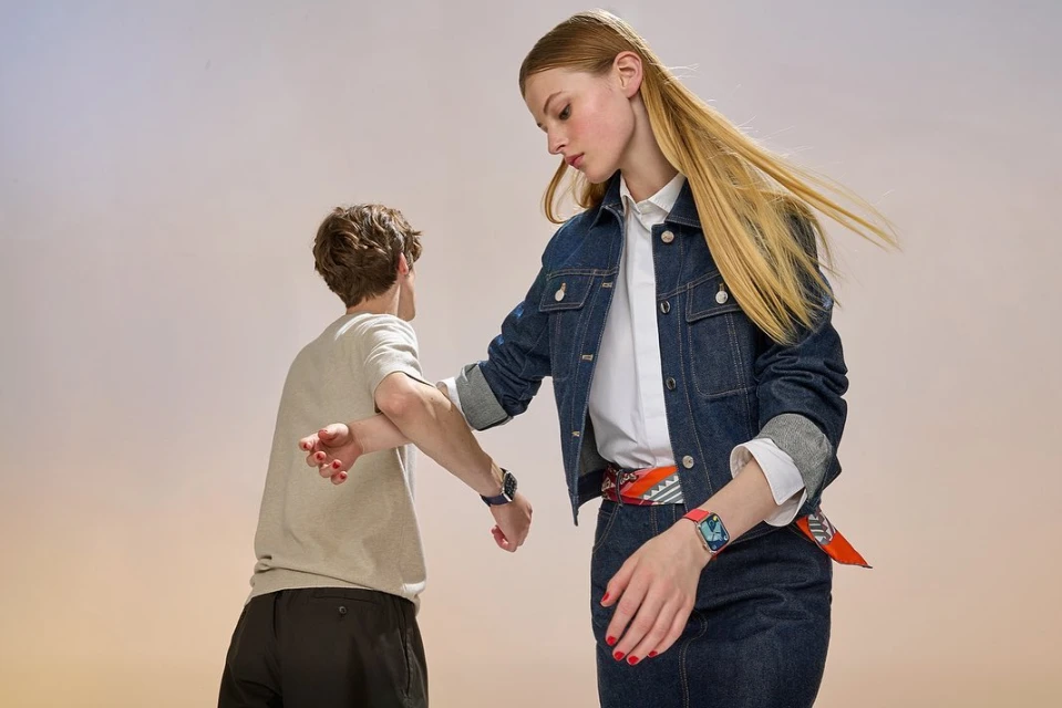 Two people wearing smart watches. A woman in denim and a patterned scarf, and a man in a beige t-shirt are shown in a studio setting.