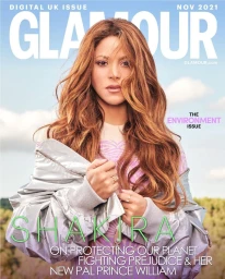 Magazine cover featuring singer Shakira with long brown hair wearing a metallic silver jacket against an outdoor sky background