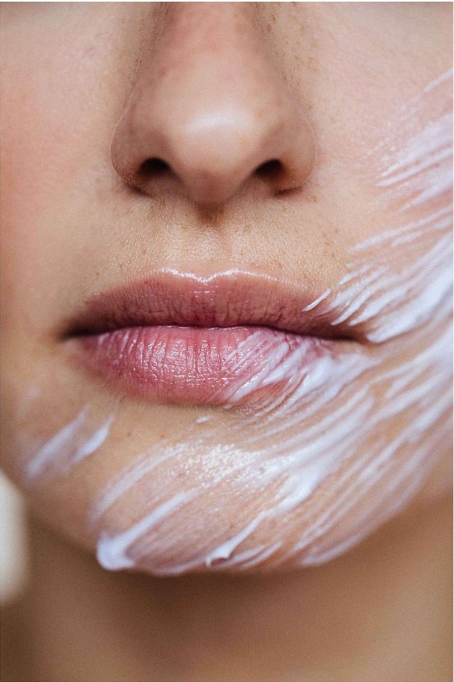 Close-up portrait of an adult female with fair skin, featuring a partial face view of her nose, mouth and cheek covered in a white creamy substance.