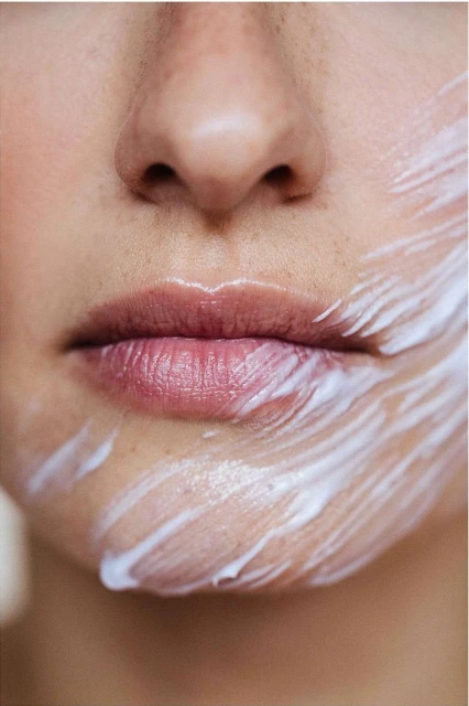 Close-up portrait of an adult female with fair skin, featuring a partial face view of her nose, mouth and cheek covered in a white creamy substance.