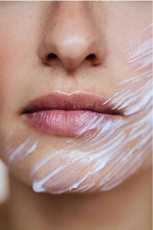 Close-up portrait of an adult female with fair skin, featuring a partial face view of her nose, mouth and cheek covered in a white creamy substance.