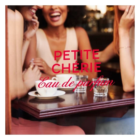 Three women are sitting at a cafe table. The table has coffee cups, a drink glass, and the words 'Petite Cherie Eau de parfum'.