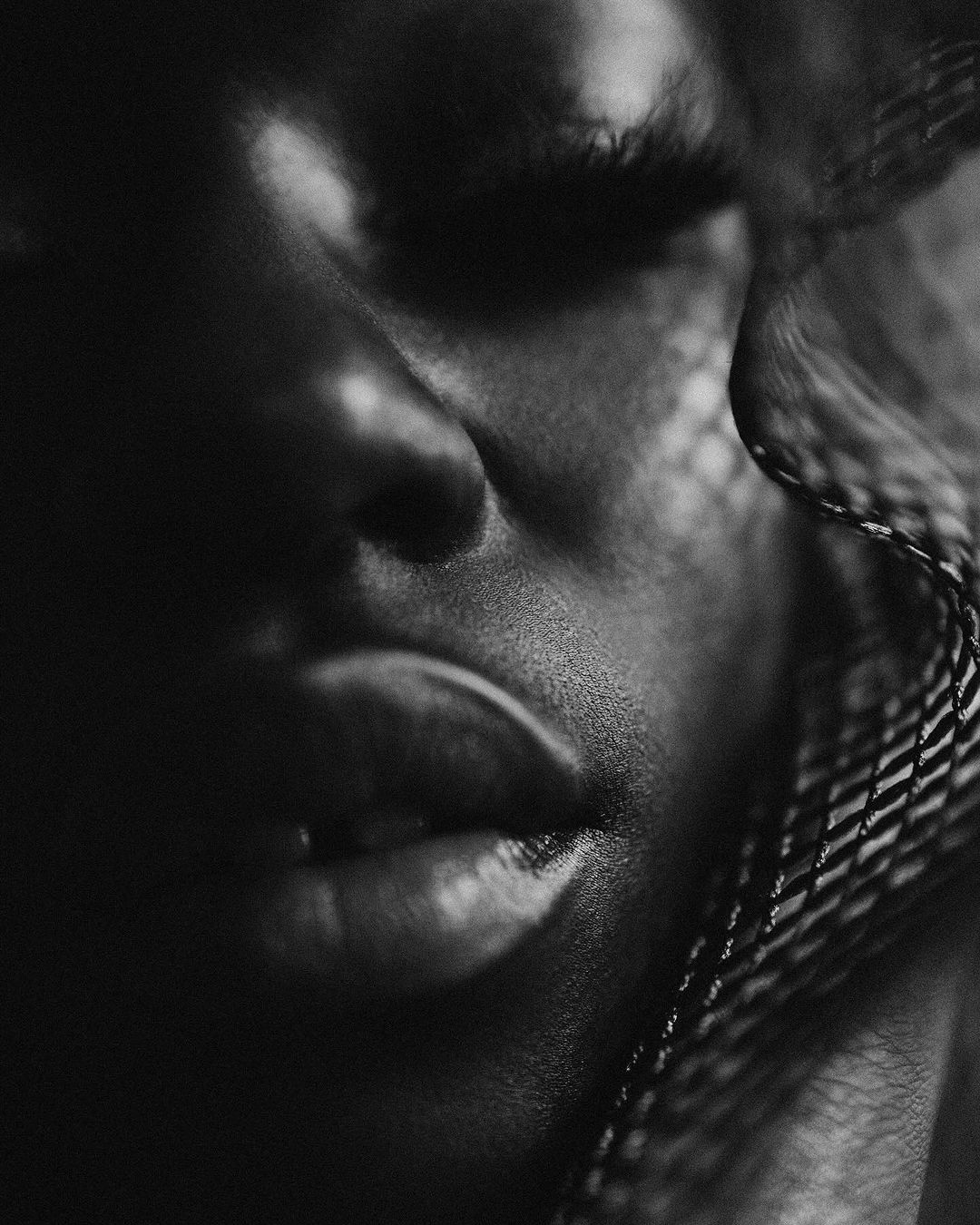 Monochrome close-up portrait of an African American adult female model with eyes closed, featuring dramatic chiaroscuro lighting.