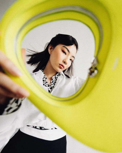 Asian woman in stylish white shirt and black skirt poses indoors with a yellow purse, creating a fashionable and eye-catching portrait.