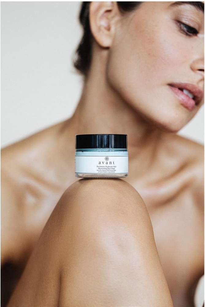 Close-up shot of a light-skinned female with a skin cream jar resting on her knee, set against a light background in a beauty context.