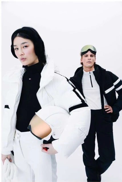 Two fashion models pose against a bright white backdrop, showcasing winter ski attire and accessories, including jackets, goggles, and gloves.