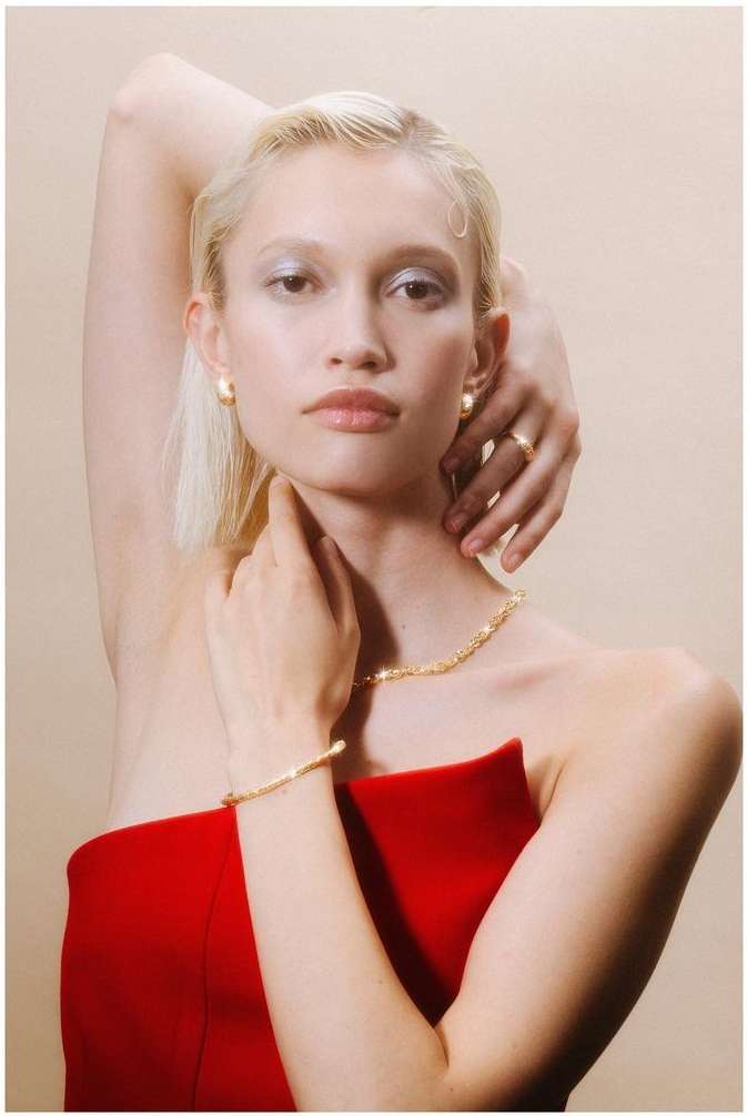 Close-up portrait of a blonde woman in a red strapless top wearing gold jewelry, photographed by Lucie Sassiat in Paris.