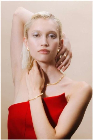 Close-up portrait of a blonde woman in a red strapless top wearing gold jewelry, photographed by Lucie Sassiat in Paris.